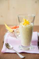 fresh smoothies in glass glass with banana, orange, mango, on wooden background.