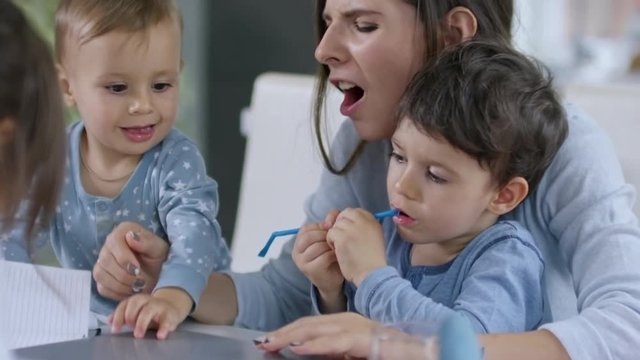 Mother trying to type something on laptop computer and looking after three children at the same time, one of them closing laptop lid and accidentally pinching mother's finger