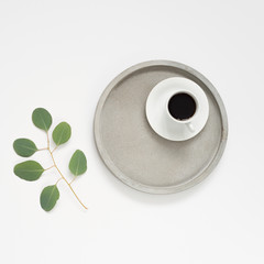 Minimalistic flat lay. White background, grey concrete tray , eucaluptus greenery and coffee