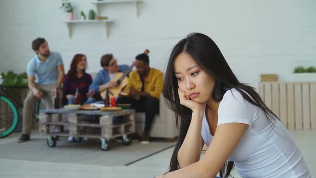 Young asian girl feels upset and isolated while her flatmates celebrating party at home indoors