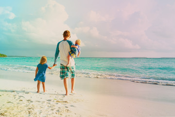 father and two kids walking on beach