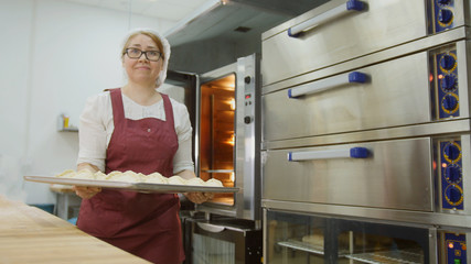Woman puts raw meat pies in the stove