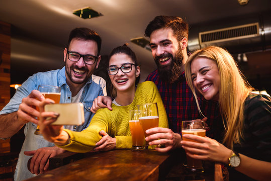 Friends in Pub drinking Beer and Looking at Smartphone