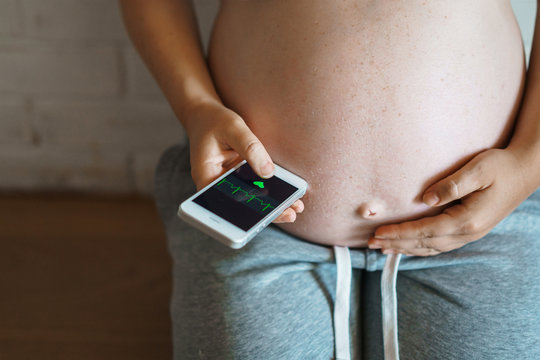 pregnant woman attached the smartphone to her stomach checking the heartbeat using a special application. Health and technology.
