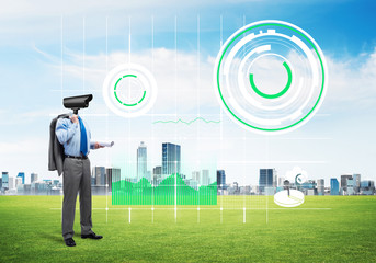 Camera headed man standing on green grass against modern cityscape