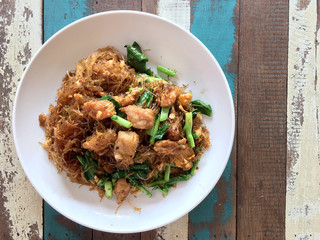 Stir fried Flat Rice Noodle with Soy Sauce and Pork in white dish on colourful wooden table in thai called 