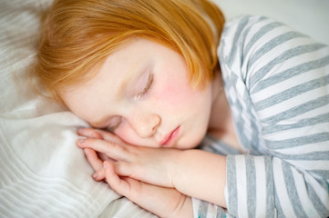 Red-haired girl sleeps with her hands on her cheek