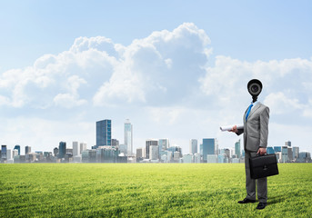 Camera headed man standing on green grass against modern cityscape