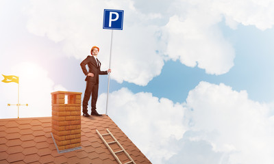 Young businessman with parking sign standing on brick roof. Mixed media