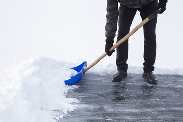 Man cleaning snow with shovel from ice surface for ice skating. Winter routine concept.