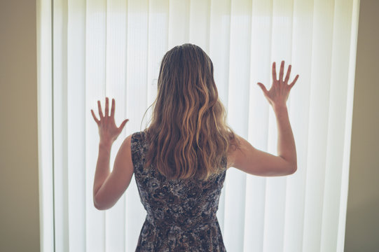 Young woman with hands up by blinds