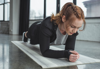 Curvy girl in gym standing in plank