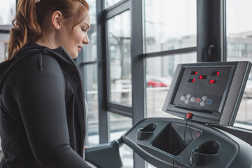 Obese girl running on treadmill in sports center