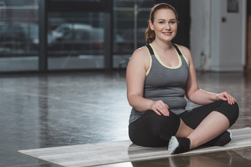 Obese smiling girl during meditation in gym
