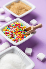 Different types of sugar with colored candy on white ceramic bowls