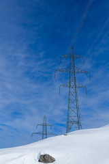 two electricity pylons in winter, snow, stone, sunny blue cloudy sky