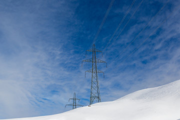 two electricity pylons in winter, snow, sunny blue sky, clouds