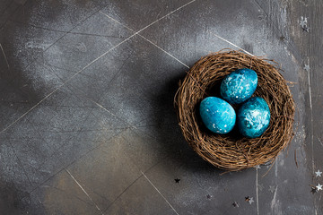 Easter eggs in nest painted by hand in blue color on dark background