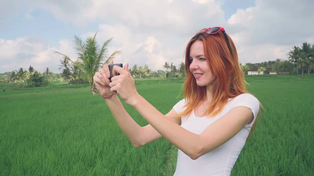 Young caucasian woman filming green lush rice field with phone and taking selfie in Bali, Indonesia