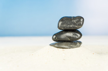 Fototapeta na wymiar Three black stones in the sand, blue sky background