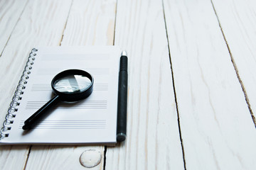 Magnifier, notebook, pen on a white wooden backdrop