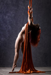 Beautiful nude dancer on aerial silk, graceful contortion, acrobat performs a trick on a ribbons