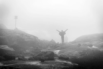 Silhouette of young woman in raincoat walking along the plateau through the foggy place on the way to Kjeragbolten, Norway.
