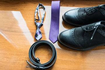 The groom's and a dog’s wedding accessories. Lilac neck tie and a black leather belt and black shoes on a wooden background.
