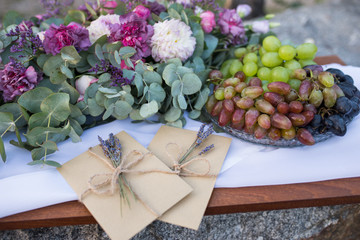A tray with grape and wedding invitations in the craft envelopes with a few branches of lavender near the flower composition. Wedding concept. Wedding accessories. Invitations 