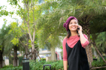 travel, business trip, people and technology concept - happy Young woman with travel bag and and talking on smartphone on city street
