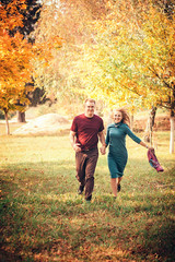 Fototapeta premium Young couple in love holding hands and running through a park on a sunny autumn day