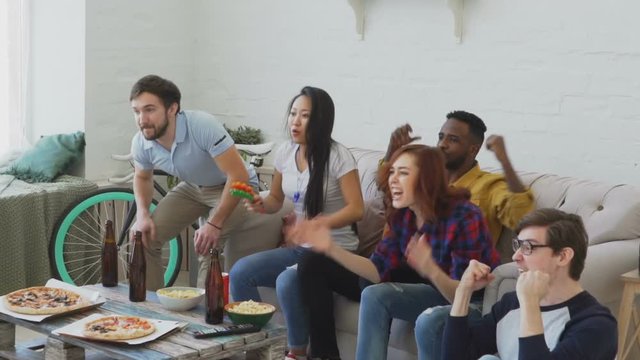 Slow motion of group of happy friends watching sports game on TV at home. They are yelling while their favorite team win competition