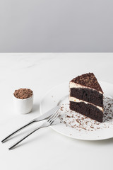 Grated chocolate in bowl with cake on plate on white surface