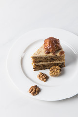 Cake on white plate surrounding by walnuts on table