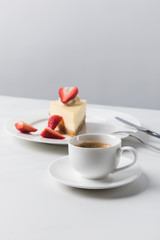 Cheesecake with strawberries on plate and cup of coffee on foreground