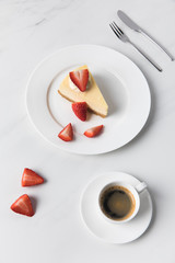 Coffee cup with cheesecake and sliced strawberries on plate