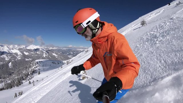 male skier with orange ski helmet skiing in fresh deep snow off piste on sunny winter day with clear blue sky in austrian mountains in 4K
