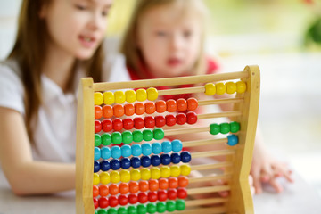 Two cute little girls playing with abacus at home. Big sister teaching her sibling to count. Smart child learning to count.