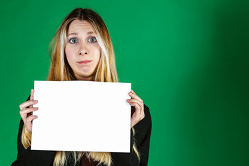 Attractive blonde business woman holding white banner with copy space for additional text or graphic. Confused model. Girl is posing on a green background