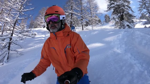 skier with orange helmet skiing in fresh snow off piste between trees on sunny winter vacation day 4K selfie pov
