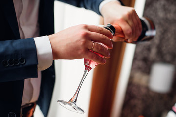 groom pours red champagne from a bottle into a close-up glass