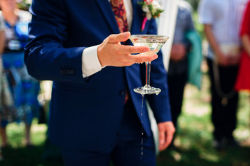 hand with a glass of shedding Martini in the hand of the groom at the wedding ceremony