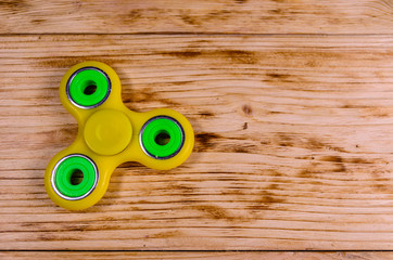 Yellow fidget spinner on wooden desk. Top view
