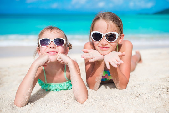 Adorable little sisters at beach during summer vacation lying on warm sand. Portrait of kids on white beach