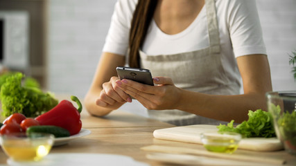 Obraz na płótnie Canvas Woman choosing salad recipe on smartphone at the kitchen, cooking application