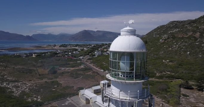 4K high quality aerial video sunny day view of historical Slangkop lighthouse built in 1914 and Kommetjie town in the background near beach at sea shore in Western Cape near Cape Town, South Africa