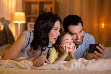 happy family with smartphone in bed at night