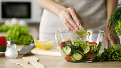 Obraz na płótnie Canvas Female hands adding olive oil to fresh vegetable salad, vegetarian lifestyle