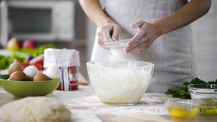 Woman hands sieving flour over glass bowl with dough, adding baking ingredients