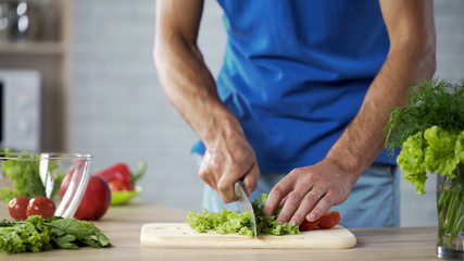 Obraz na płótnie Canvas Husband cutting fresh salad on board for healthy family lunch, cooking help